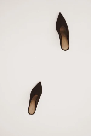 Pair of brown, pointed-toe heeled mules on a white surface, showcasing minimalist style and elegant footwear fashion.