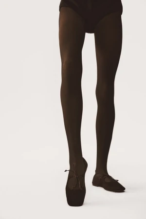 A close-up studio shot of a ballet dancer's legs and feet wearing black tights and ballet shoes against a white backdrop. Focus on pose.