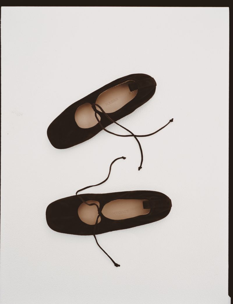 Two black ballet shoes, or pointe shoes, sit against a white background. The shoes are angled with laces and a plain design.