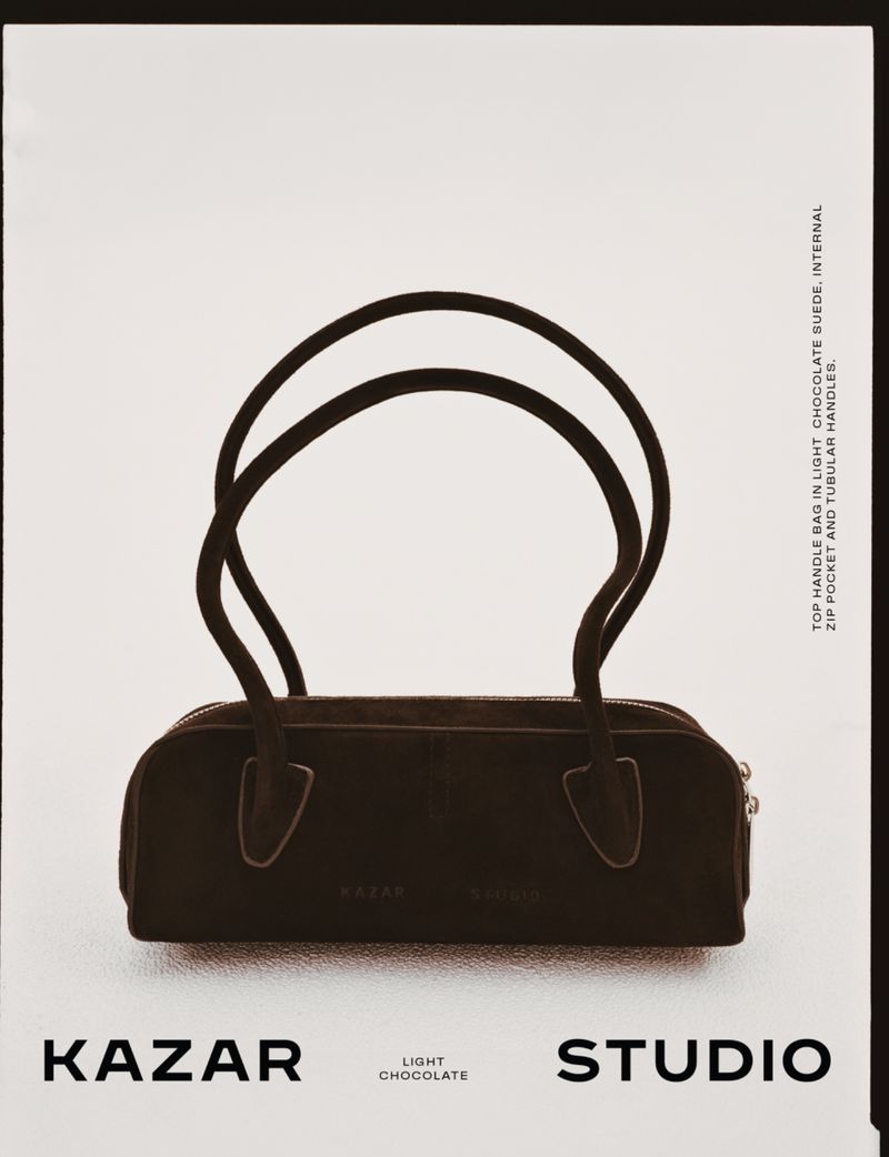 Dark brown Kazar brand top handle bag on a white background, featuring two tubular handles and minimal design, ideal for fashion.