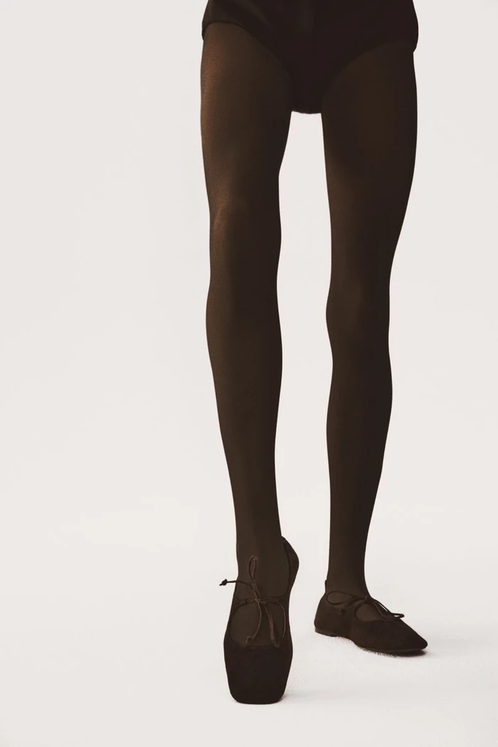Close-up of model legs wearing dark tights and ballet flats against a seamless white background for Kazar Studio.