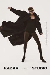 Model Diana Skowron in a billowing black coat, black bodysuit, tights, and stiletto heels against a white studio background.