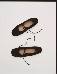 A pair of black square-toe ballet flats with thin lace-up ties arranged on a plain white backdrop.