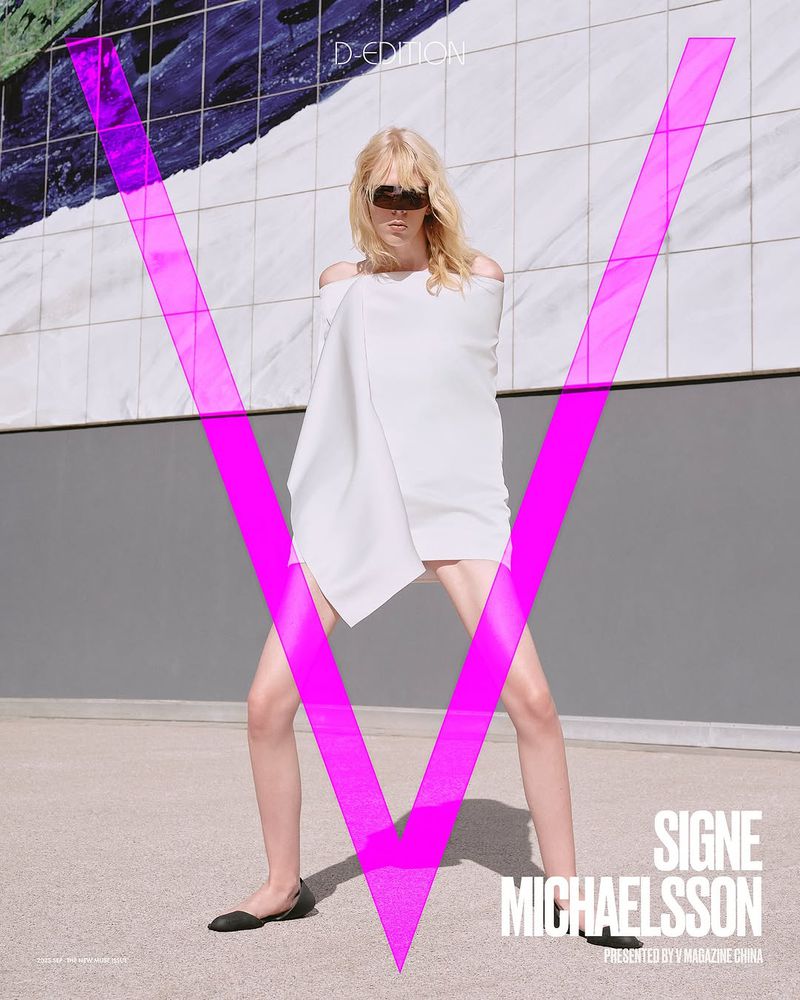 Fashion editorial shot of a blonde adult female wearing a white dress and sunglasses, standing outdoors with a stylized pink 'V' overlay.