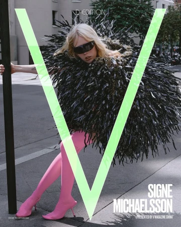 Editorial fashion shot of a woman in a feather coat and pink boots, posing against an urban street with building and large letter V.