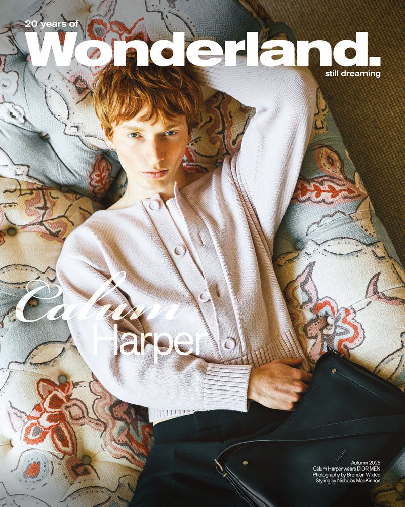 Magazine cover featuring a person with red hair, wearing a pink cardigan, lying on a floral patterned sofa, holding a black bag.