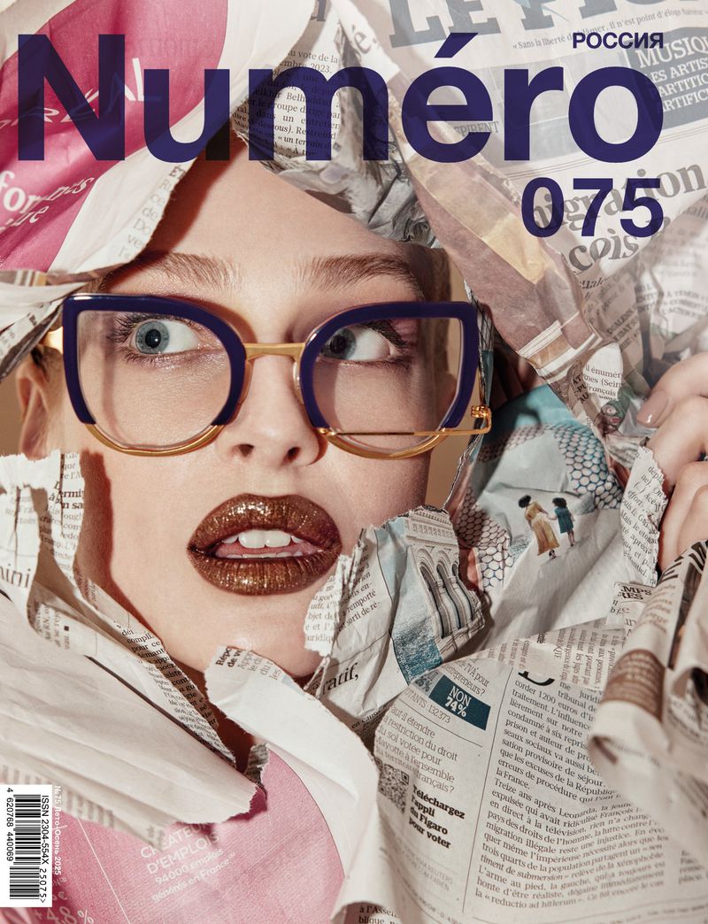 Fashion magazine cover featuring a woman wearing blue glasses and wrapped in newspaper, staring off-camera with a surprised expression.
