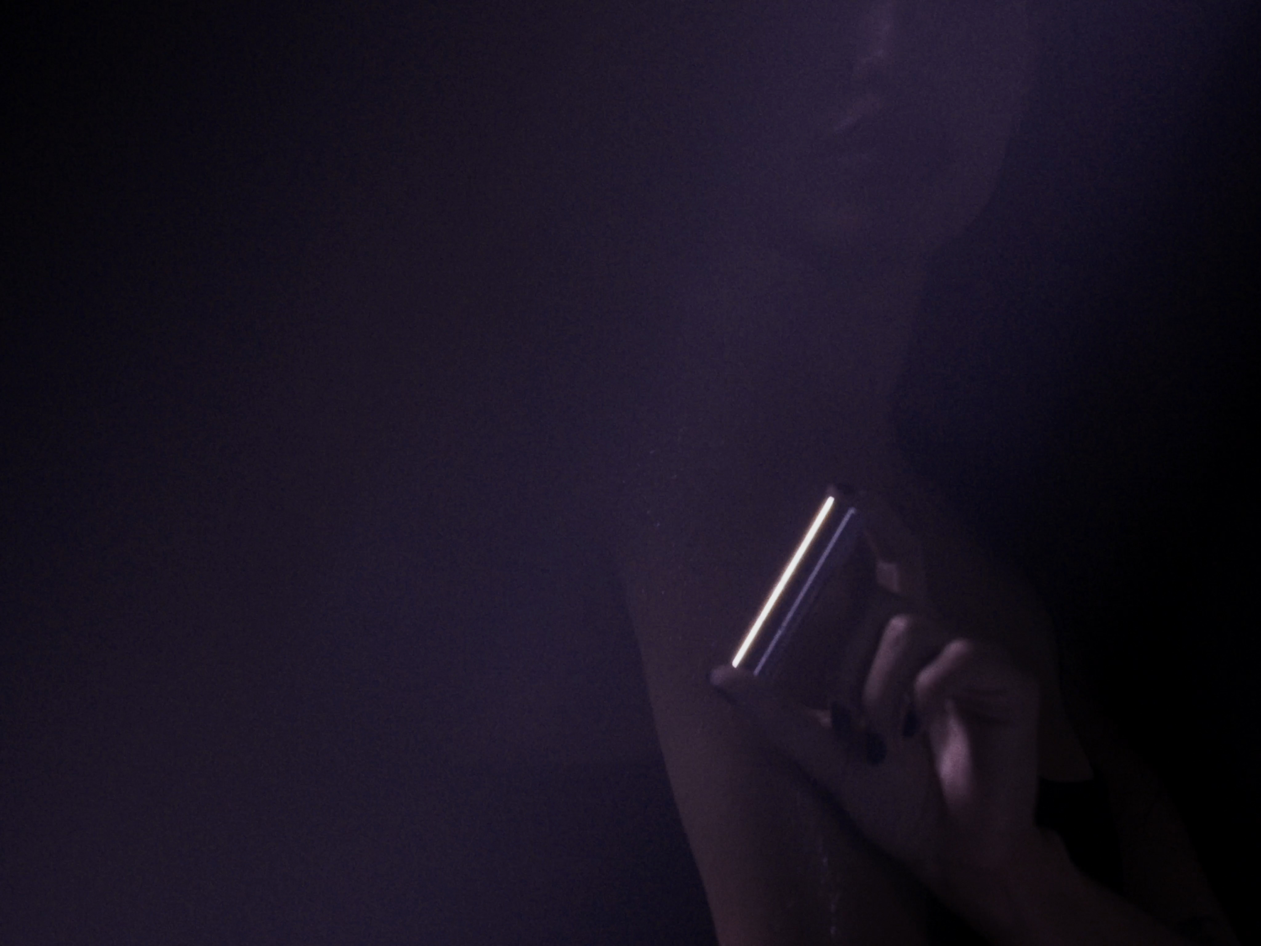 Woman's hand holds lit mobile phone in the dark, showing its screen in a portrait orientation, with dark nail polish, and dark lighting.