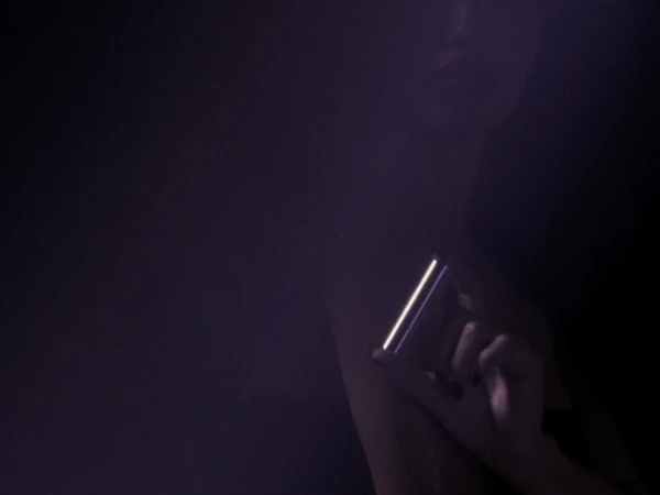 Woman's hand holds lit mobile phone in the dark, showing its screen in a portrait orientation, with dark nail polish, and dark lighting.