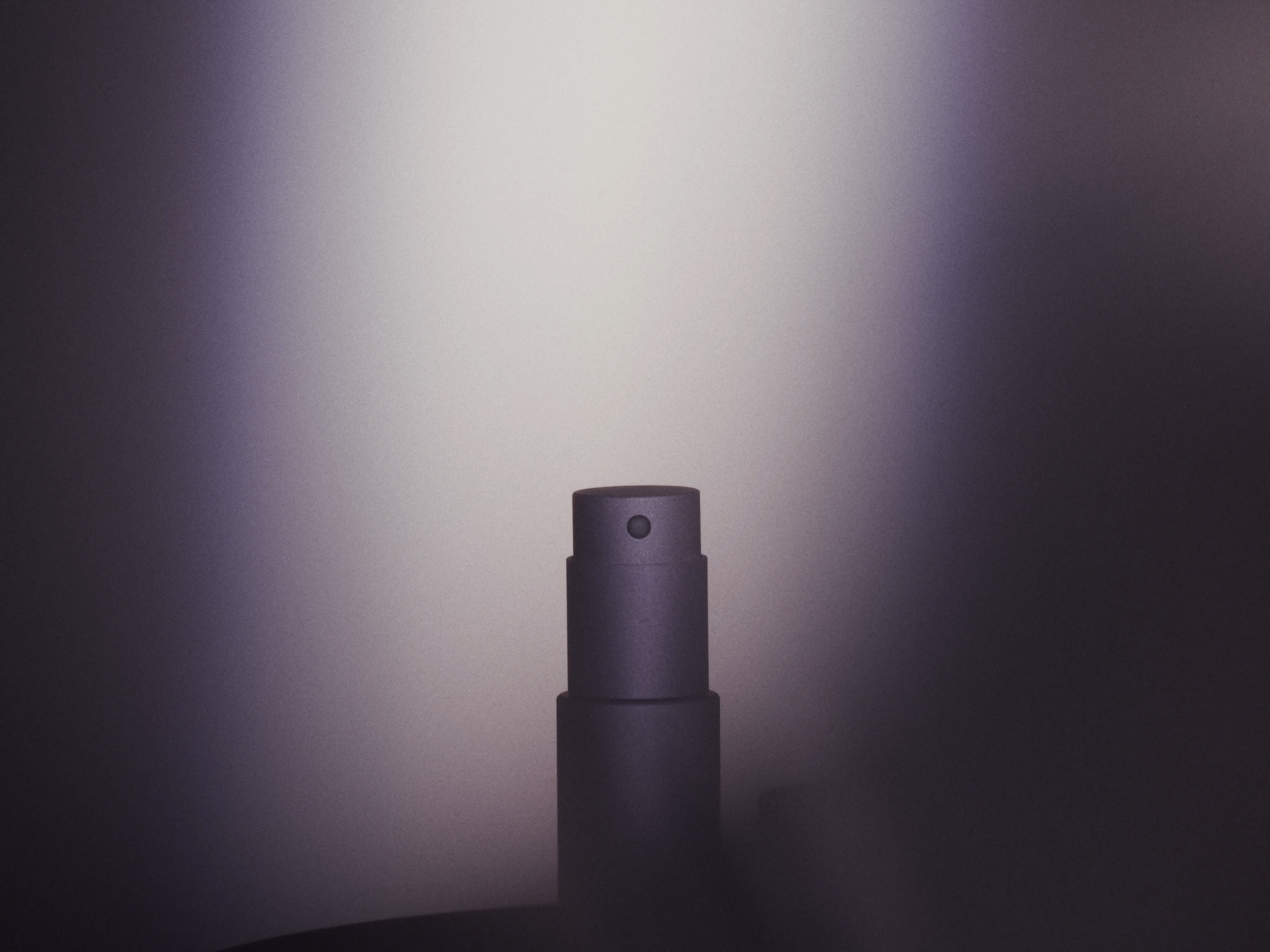 Close-up studio shot of a sleek grey perfume bottle. The focus is on the bottle's minimalist design against a gradient grey backdrop.
