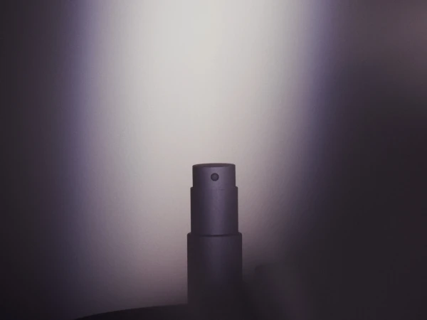 Close-up studio shot of a sleek grey perfume bottle. The focus is on the bottle's minimalist design against a gradient grey backdrop.