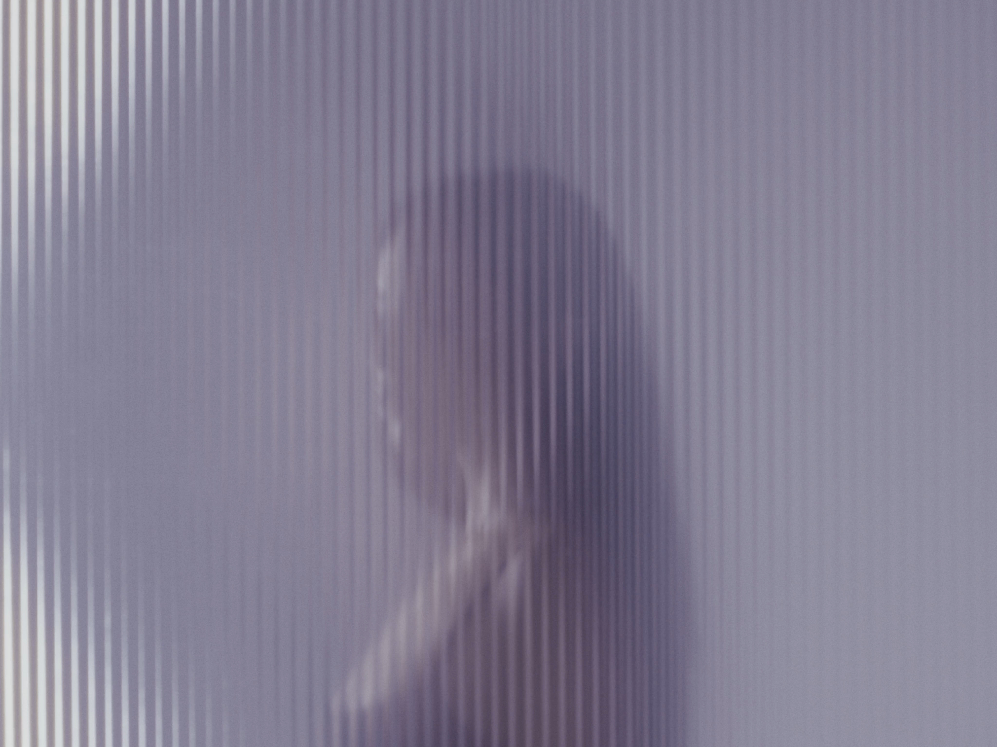 Abstract portrait of a woman silhouetted behind reeded glass, creating soft, diffused light and a dreamy, ethereal visual effect.