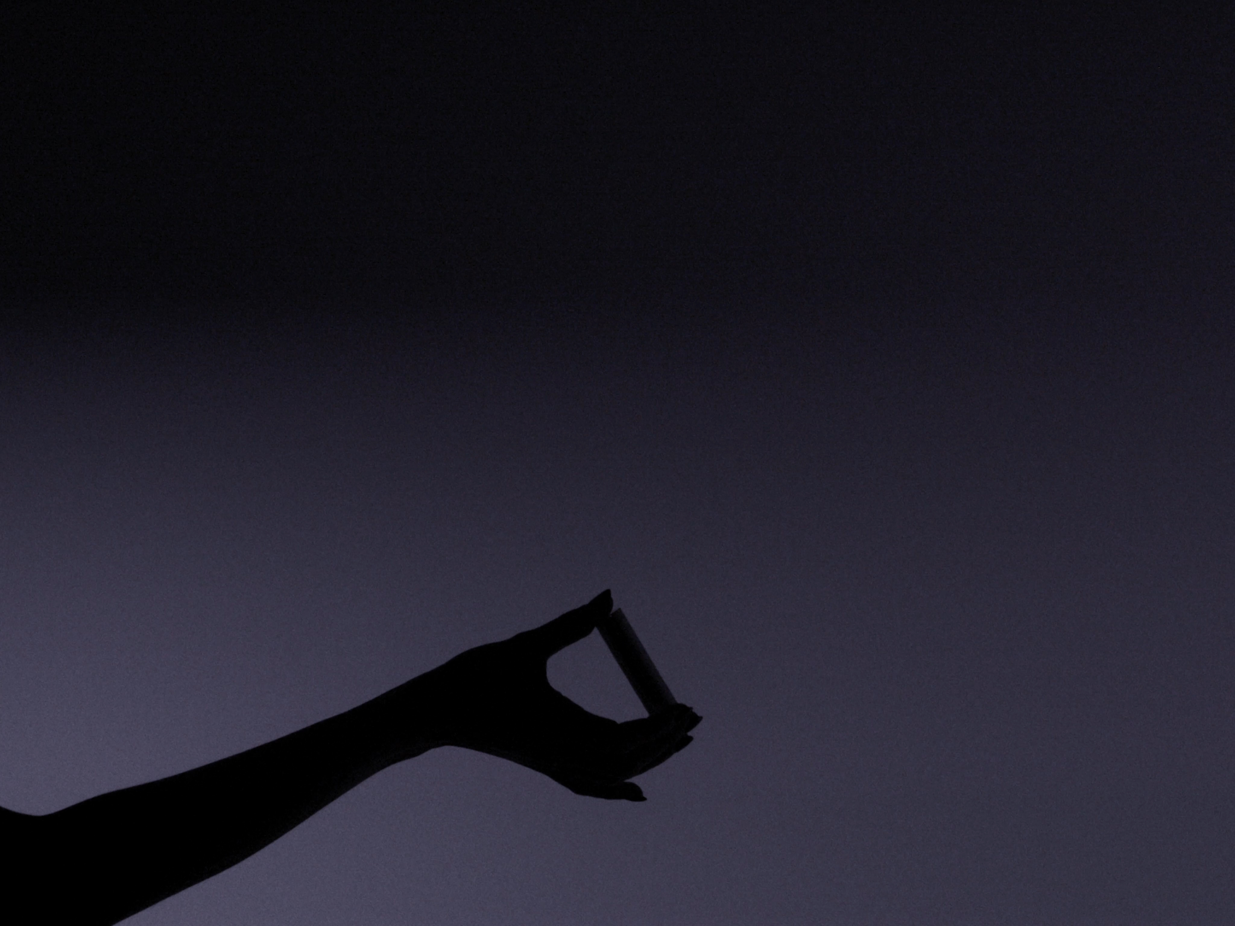 Silhouette of a hand holding a cigarette against a purple-gray gradient background with soft lighting creating a moody atmosphere.
