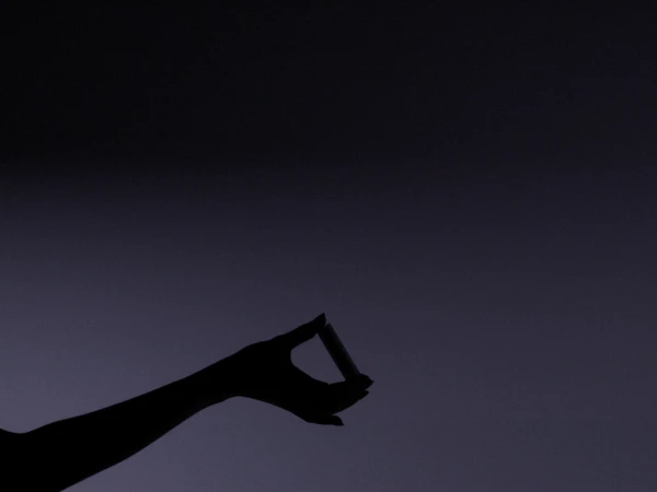 Silhouette of a hand holding a cigarette against a purple-gray gradient background with soft lighting creating a moody atmosphere.