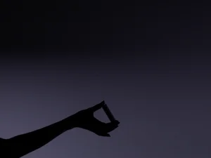 Silhouette of a hand holding a small cylindrical capsule against a dark muted purple gradient background.