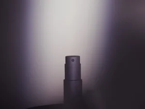 A close-up of a dark matte fragrance spray nozzle positioned centrally against a soft moody gradient background.