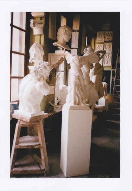 Photo studio interior filled with plaster sculptures, including busts on stands, against a backdrop of windows and architectural details.