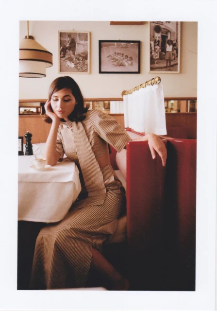 Young woman in striped dress sits in a red booth at a restaurant with black and white framed photos on the wall.