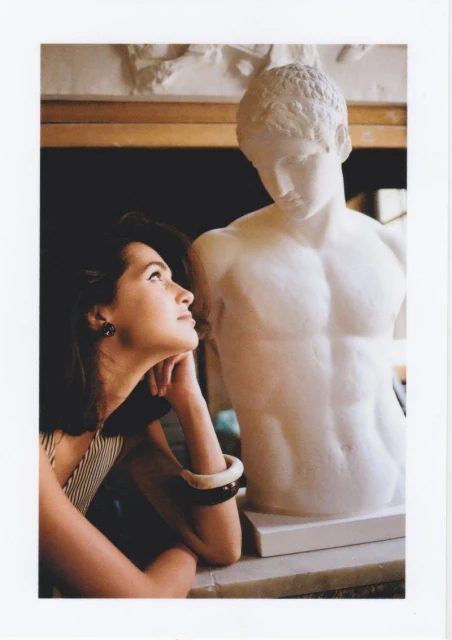 Elegant woman gazes at a white marble sculpture in an indoor setting, creating a harmonious blend of classic art and modern beauty.