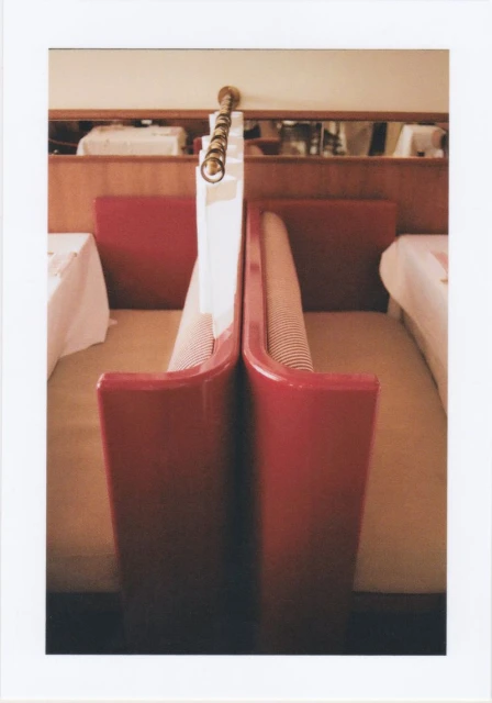 Interior view of a red booth with a striped seat in a brightly lit room, featuring a wooden wall, neutral-colored carpet, and tables nearby.