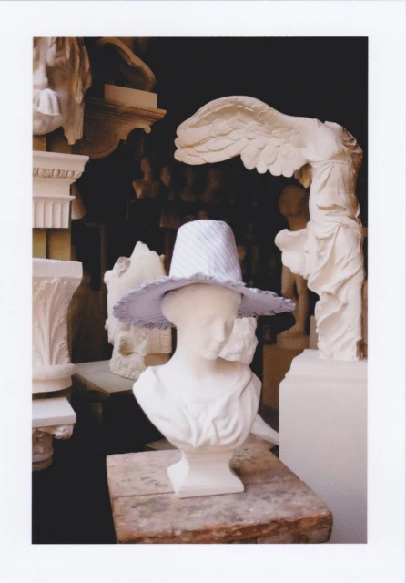 Bust of a Greco-Roman figure wearing a hat, surrounded by similar sculptures in a dimly lit museum or indoor space.