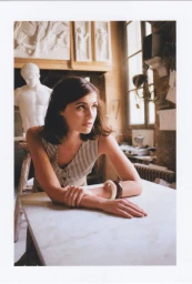 Portrait of a woman wearing a striped top leaning on a marble table in an art studio with classical sculptures