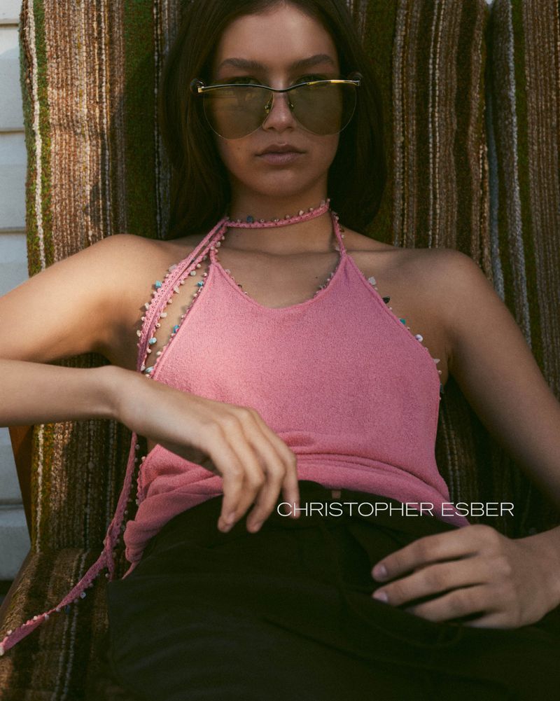 Woman in sunglasses and pink top lounges on a striped surface. Portrait shot with natural light, showcasing a relaxed, summery aesthetic.