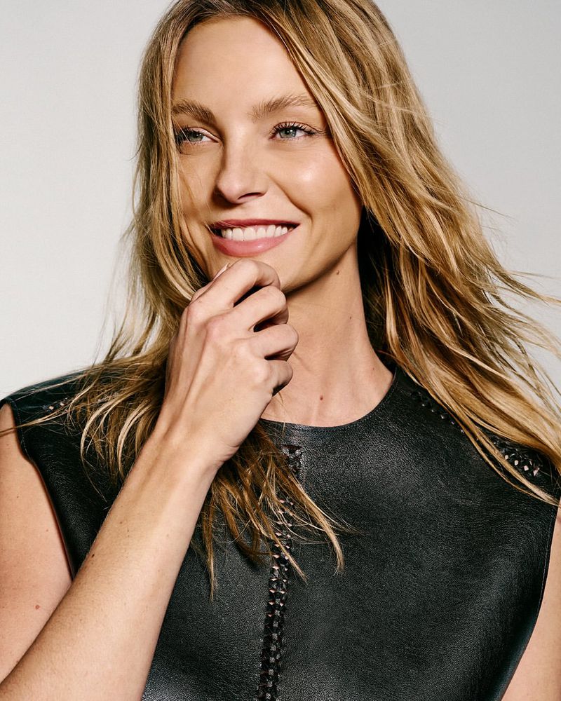 Portrait of a blond woman with a warm smile, wearing a black sleeveless top, posing in a studio with soft lighting.
