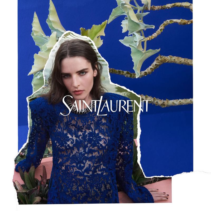 Fashion shot featuring a woman in a blue lace top posing against a blue background with foliage and the Saint Laurent logo.