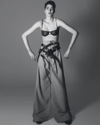 Model Snezana Gasic posing in a black lace bra and oversized wide-leg trousers with multiple leather belts in a studio setting.