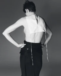 Model Snezana Gasic seen from behind wearing a white open-back top and black draped skirt against a studio backdrop.