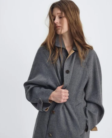 Adult female in a gray wool coat with brown buttons in a studio environment, posing indoors. The coat has tan colored lining inside.