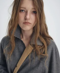 Close-up portrait of a female model wearing a grey wool coat against a plain white background.