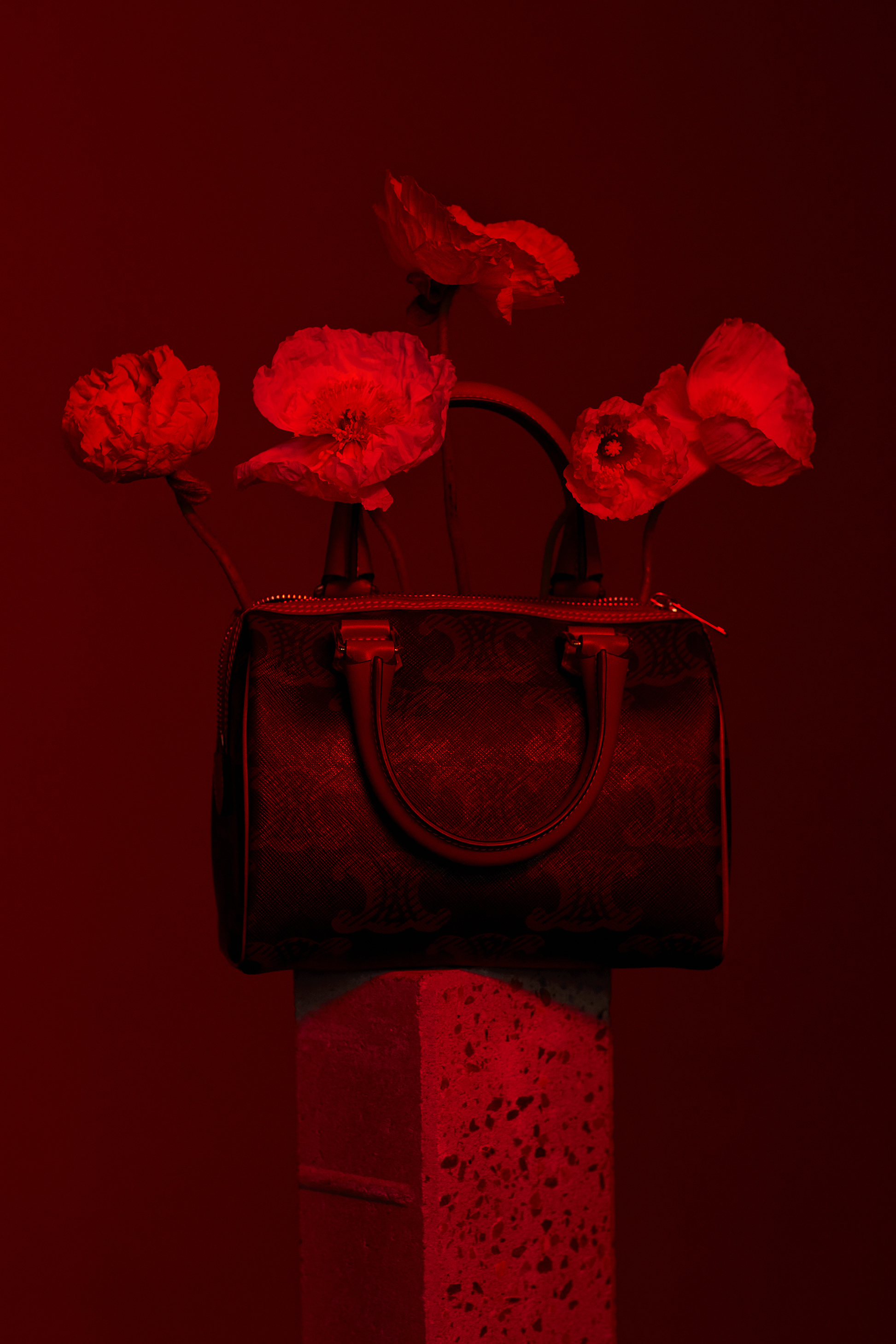 Fashionable satchel-style handbag on a pedestal with floral accents, all under a red color cast, creating a striking and stylish image.