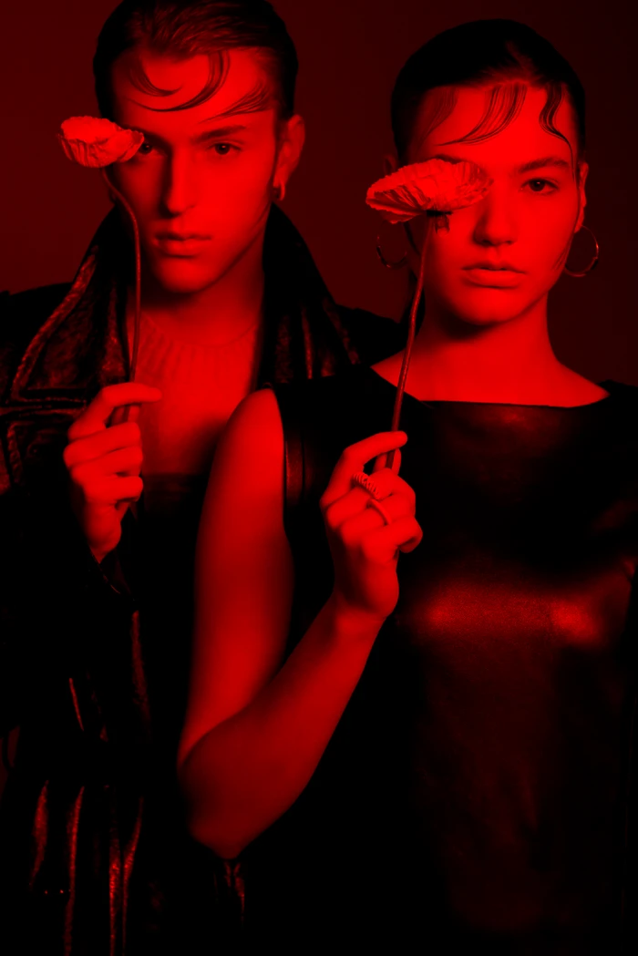 Two models bathed in deep red light holding poppies over one eye for Base cast by Milos Mlynarik.