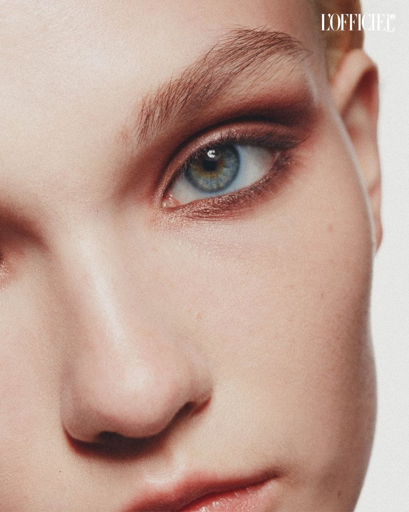 Close-up shot of a female adult face with visible eye makeup and natural skin texture against a bright studio background.