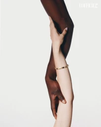 Two intertwined arms with contrasting skin tones wearing a gold bracelet against a pure white seamless background.