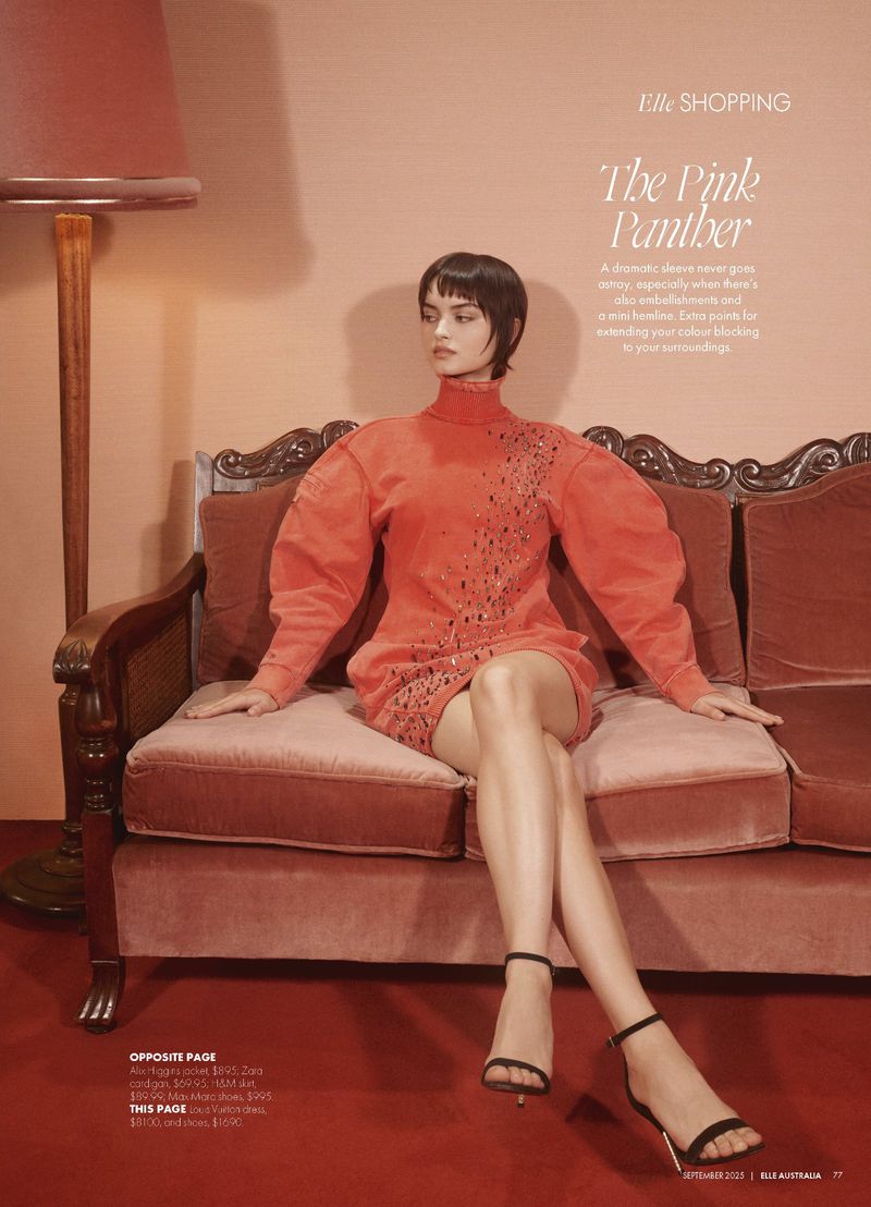 A woman models a red dress on a vintage couch in a studio. She wears heels, creating a sophisticated fashion moment.