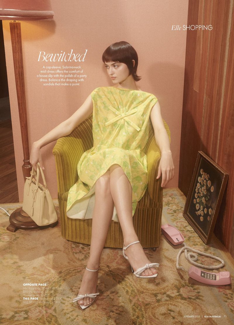 A woman in a patterned yellow dress sits in an armchair with a bag and sandals, set against a wood-paneled wall with a 70s aesthetic.