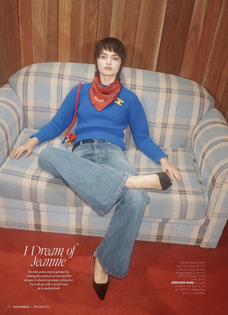 Greta Hajwos sits on a plaid sofa wearing a vibrant blue knit sweater, flared denim jeans, a red neck scarf, and black pointed heels.
