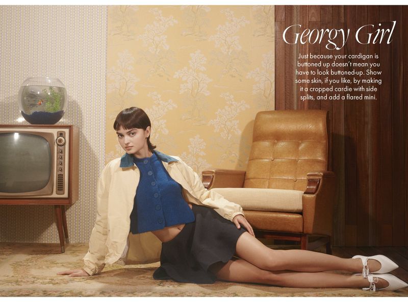 A woman in a blue top and dark skirt poses on the floor next to a vintage TV and chair, creating a retro fashion editorial shot.