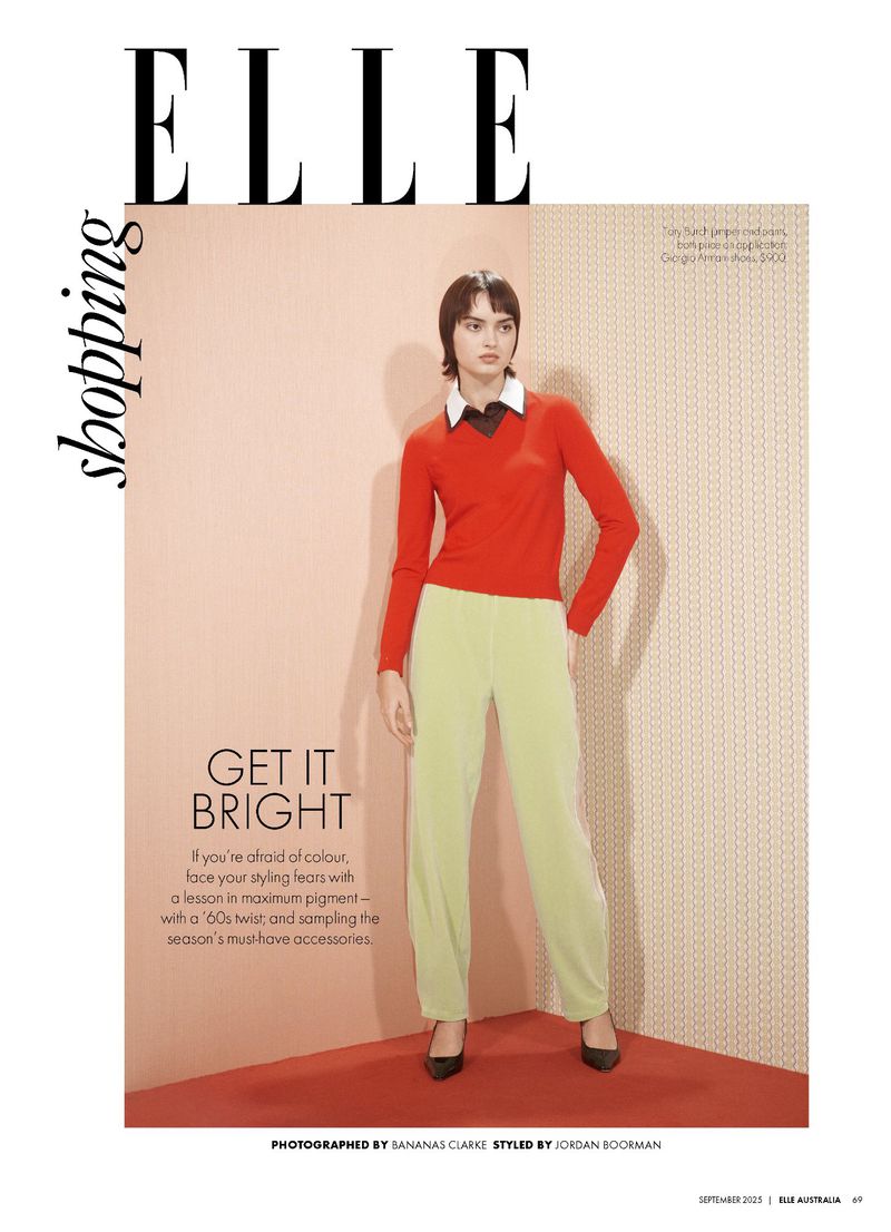 Fashion editorial shot of a female model in a red top and light green pants against a peach-toned wall with geometric-patterned paneling.