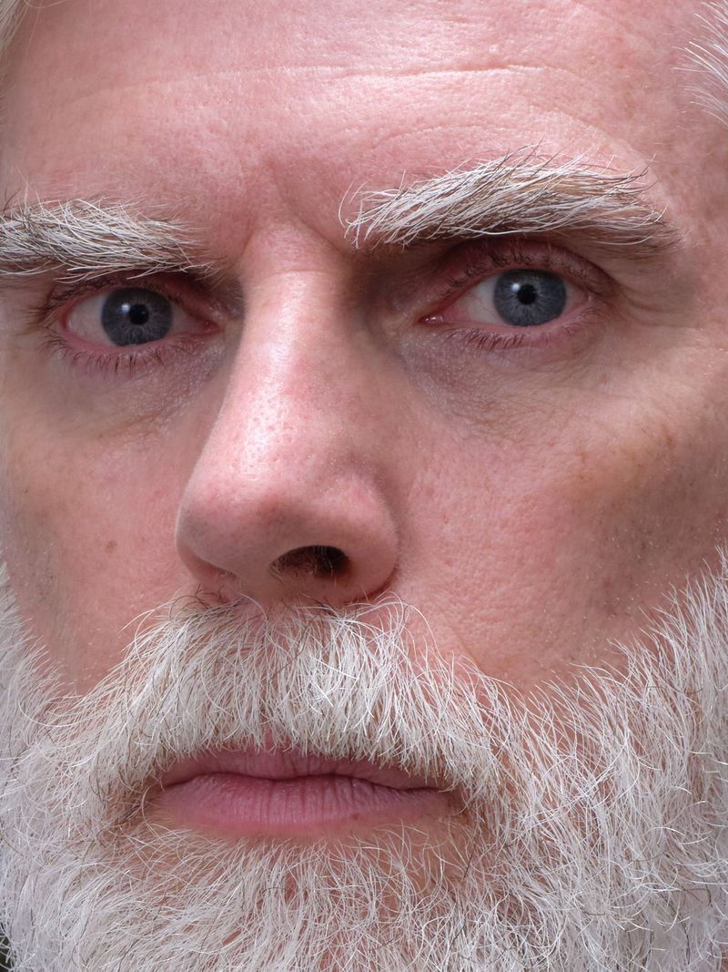 Close-up portrait of an elderly man with a white beard and blue eyes, captured with soft lighting and a shallow depth of field.