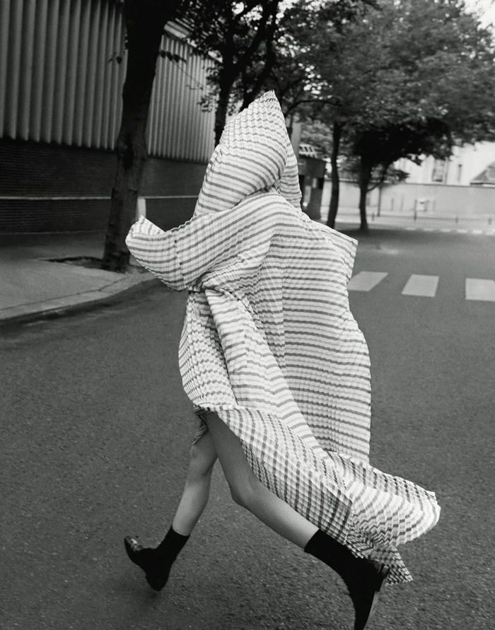 Model Mauve Dupuy completely draped in an oversized patterned hooded cape while running down an urban street in black and white.
