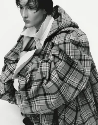 Model wearing a plaid hooded coat over a white shirt against a plain white background for T - Le magazine du Temps