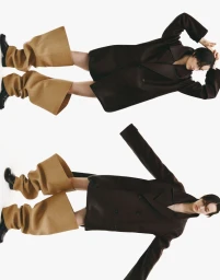 Model Mauve Dupuy in an oversized dark coat and wide camel leg covers against a white seamless studio backdrop.