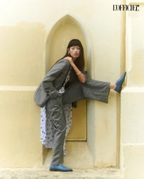 Tatiana Torres posing in a grey suit and polka dot skirt inside a yellow arched alcove for L'Officiel Chile's Silent Bloom.