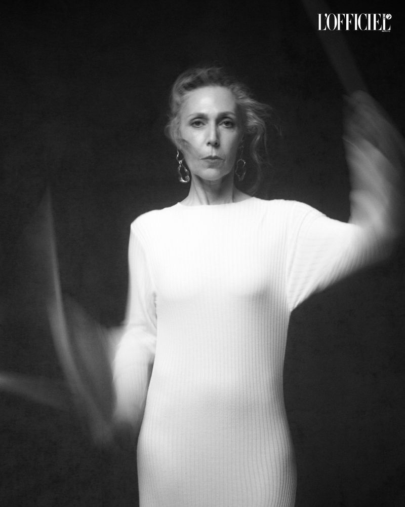 Elegant portrait of a mature woman in a white dress against a dark backdrop, showcasing fashion and understated beauty in a minimalist style.