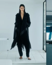 Model in black coat standing in a bright minimalist interior for Helmut Lang Pre-Fall 2025 editorial