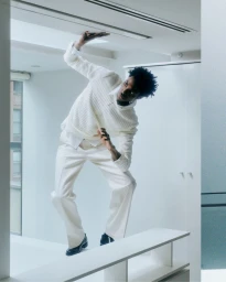 Model wearing a white sweater and trousers posing in a white interior for Helmut Lang pre-fall 2025 edit